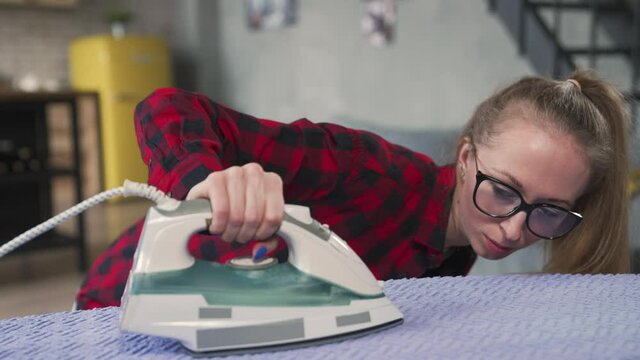 Young woman attentively looks at iron while ironing