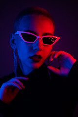 Portrait of a young woman with a short male haircut in sunglasses in neon light in the studio