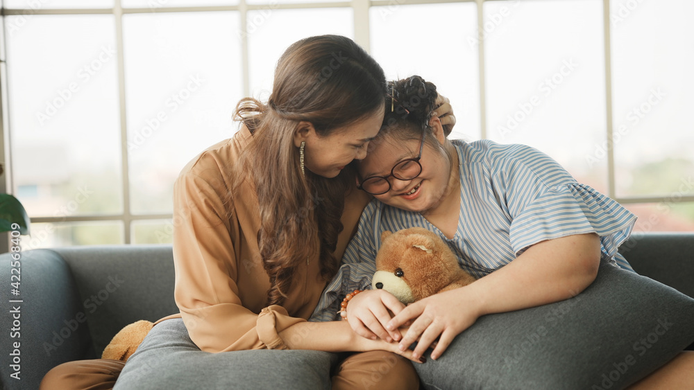 Wall mural mother supporting sweet down syndrome daughter to learn and relax from the internet, embracing child