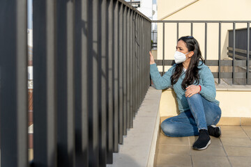 Woman wearing protective face mask sitting in the terrace and looking at natural background.