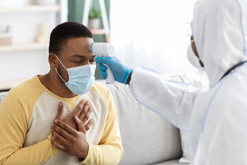 Sick black guy in face mask receiving checkup at home