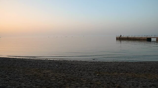 San Simon bay, Slovenia: concrete pier with calm waves hitting pebble beach at sunset. Beautiful colors at golden hour. Static shot, real time, wide angle