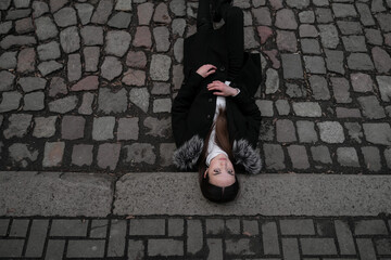 a young girl lies on the sidewalk, on the roadway, view from the top