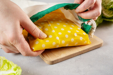 Woman hands placing sandwich wrapped in beeswax cloth into cotton bag