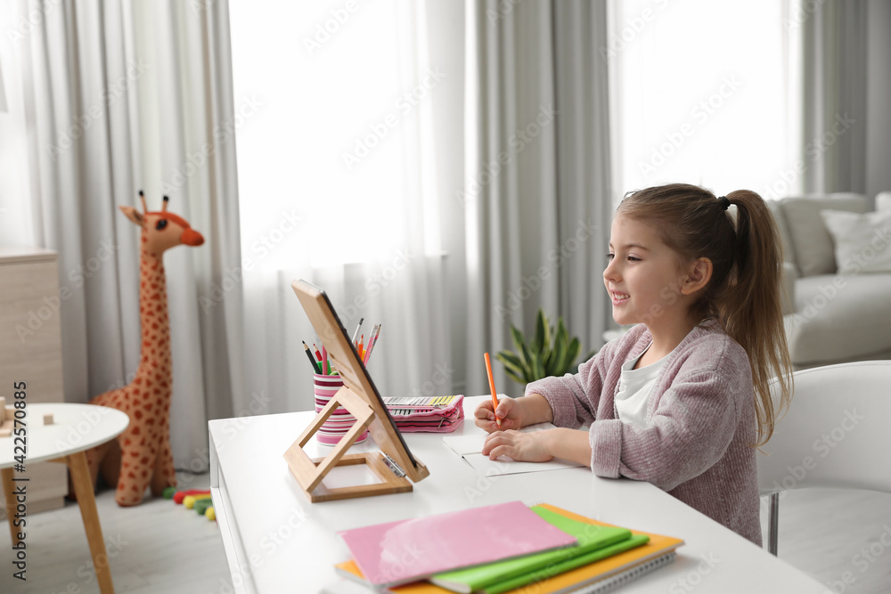 Poster Adorable little girl doing homework with tablet at table indoors