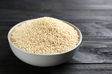 Sesame seeds in bowl on black wooden table