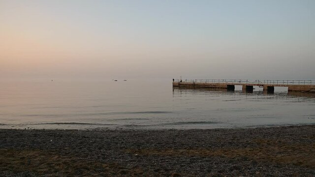 San Simon bay, Slovenia: concrete pier in winter. Calm waves hitting pebble beach at sunset. Beautiful colors at golden hour. Static shot, real time, wide angle