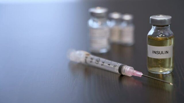 A slider dolly shot of a generic insulin vial. A doctor, nurse, or pharmacist picks up a hypodermic needle.  	