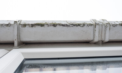 Dirty clogged white plastic pvc gutters and drain pipes with mossy green mould on plastic fascias. ...