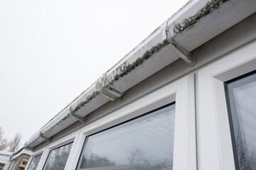 Dirty clogged white plastic pvc gutters and drain pipes with mossy green mould on plastic fascias. ...