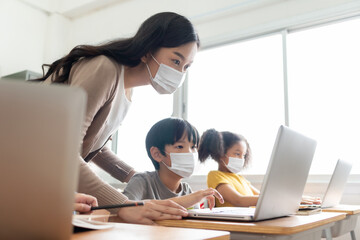 Asian Young Teacher with little boy in protective face masks using laptop for  studying in...