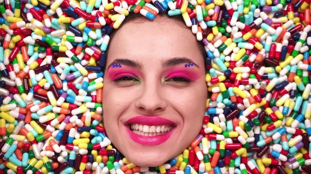 Artistic image of a beautiful woman sunk inside colored pills and capsules. 
