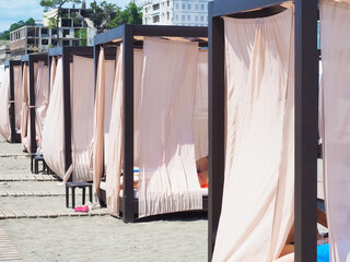Beach cabins with a metal frame and light curtains stand in a row on the sand with wooden paths