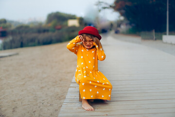 Caucasian sad girl in a hat and dress sits crying on the path in the park, children's emotions and...