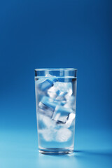 A glass with ice water and ice cubes on a blue background.