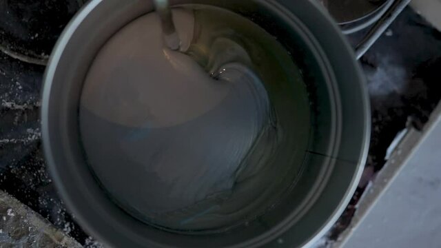 Worker mixing gray epoxy resin with the mixer in a tin bucket