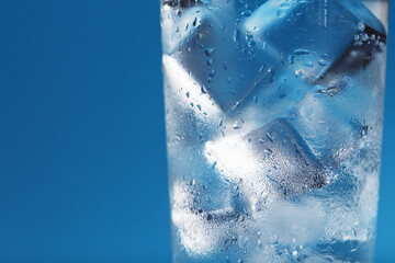 A glass with ice water and ice cubes on a blue background.