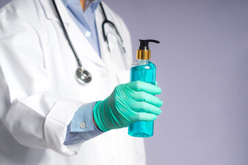 Close-up of hands doctor's wearing gloves and holding alcohol gel bottle while standing on gray background. Space for text. Concept of protection and healthcare