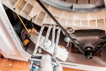 A worker removes a broken heating element from the washing machine. Close-up view of hands