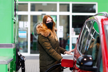Woman wear medical mask at self-service gas station, hold fuel nozzle, refuel the car with petrol...