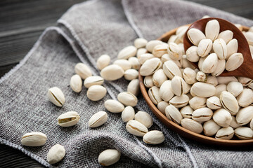 Pistachios in a wooden spoon. Wooden bowl with nut pistachios. on a wooden background, near a bag from burlap. Healthy food and snack, organic vegetarian food. (selective focus; close-up shot)