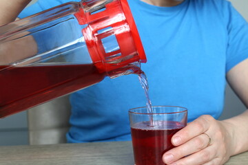 Female hands pour juice from a decanter into a glass
