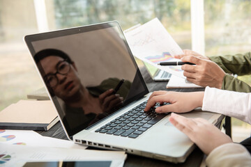 Side view of businesswoman's hands using laptop computer placed on messy office desktop. teamwork with business people analysis cost graph on desk at meeting room.