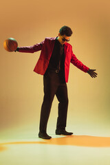 High-fashion styled man in red jacket playing basketball isolted over brown background