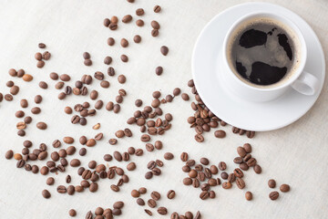 Sprinkled roasted coffee beans and a white cup of coffee. Morning coffee for breakfast