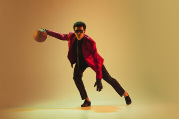 Fototapeta premium High-fashion styled man in red jacket playing basketball isolted over brown background