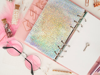 Silver key on the white page of the planner. Diary open with white and holographic page. Pink planner with cute stationery. Top view of the pink planner with stationery. Pink glamour planner