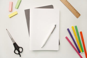 Notepad on a white background with colored pencils and felt-tip pens, rulers and scissors. The notebook lies on a plain background with space for writing. Composition of writing to-dos for the day.