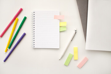An open notebook on a white background with colored pencils and felt-tip pens, a ruler and scissors. The notebook lies on a plain background with space for writing. Composition of writing to-dos for t
