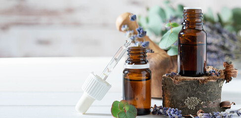 organic cosmetics concept, glass bottle with oil, pipette and lavander flowers, eucaliptus on light wooden background