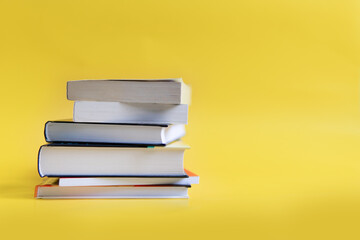 A stack of books on a yellow background. The books are on a plain background with space for writing. Composition of a reading person.