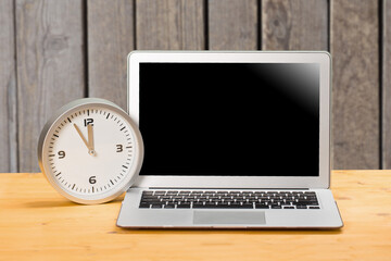 mocap Laptop and clock with arrows at five to twelve on a wooden table.