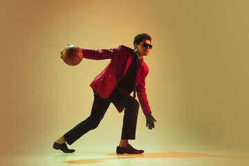 High-fashion styled man in red jacket playing basketball isolted over brown background
