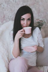 young brunette girl in pink pants and a white sweater holds a mug and saucer in her hands