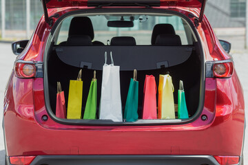 Colourful paper bags in red car trunk with. 
