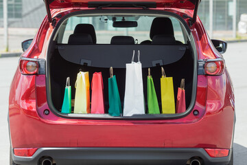 Colourful paper bags in red car trunk with. 