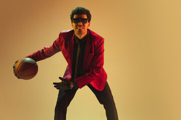 High-fashion styled man in red jacket playing basketball isolted over brown background