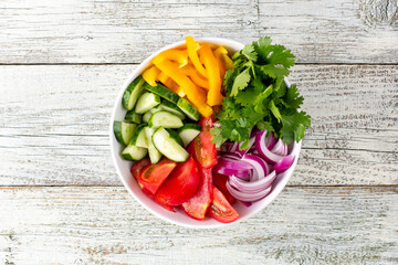 Plate of rainbow salad with different vegetables and herbs in white bowl on white wooden background