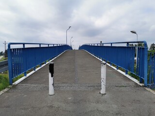 Concrete empty pavement on viaduct above the railway, with blue barriers. Cloudy weather