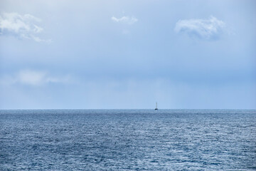 Obraz premium sailboat sails on the horizon with shimmering sea and uncertain and cloudy weather