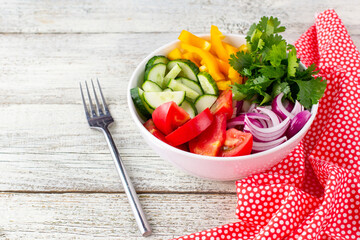 Plate of rainbow salad with different vegetables and herbs in white bowl on white wooden background