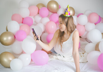 Obraz premium Photo of joyful woman smiling and taking selfie photo on cellphone with balloon. Birthday party