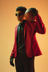 High-fashion styled man in red jacket playing basketball isolted over brown background