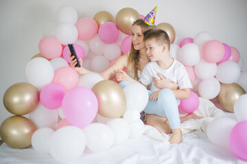 Fototapeta na wymiar Photo of joyful woman with kid boy smiling and taking selfie photo on cellphone with balloon. Birthday party