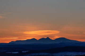Sunset behind Norwegian mountains in winter. Orange sky and snow covered woodland. Shot in Sweden, Scandinavia