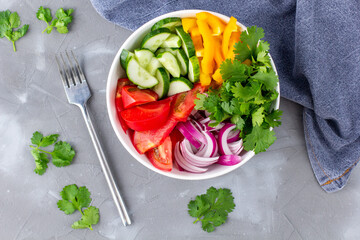 Plate of rainbow salad with different vegetables and herbs in white bowl on grey stone background